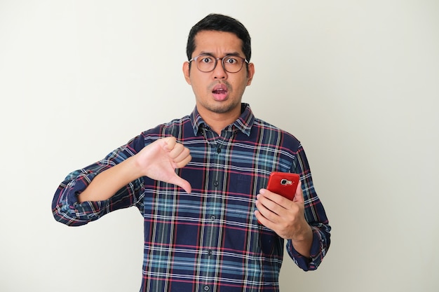Foto homem adulto asiático dá uma avaliação ruim e mostra uma expressão de decepção enquanto segura um telefone celular