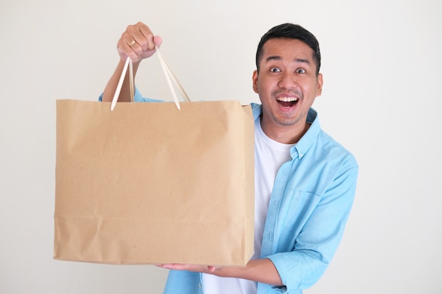 Homem adulto asiático mostrando uma expressão facial feliz enquanto mostra sua grande sacola de compras