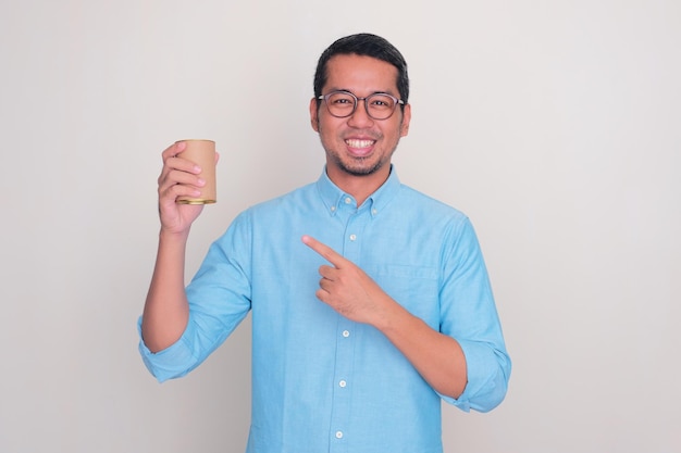 Homem adulto asiático sorrindo e apontando para a lata de bebida que ele segura