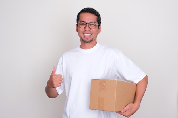 Foto homem adulto asiático sorrindo e dando o polegar para cima enquanto segura um pacote de papelão