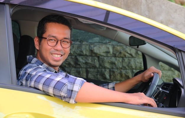 Homem adulto asiático sorrindo para a câmera de dentro de seu carro