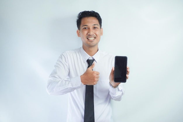 Foto homem adulto asiático vestindo camisa branca e gravata sorrindo e dando o polegar para cima enquanto segura o telefone celular