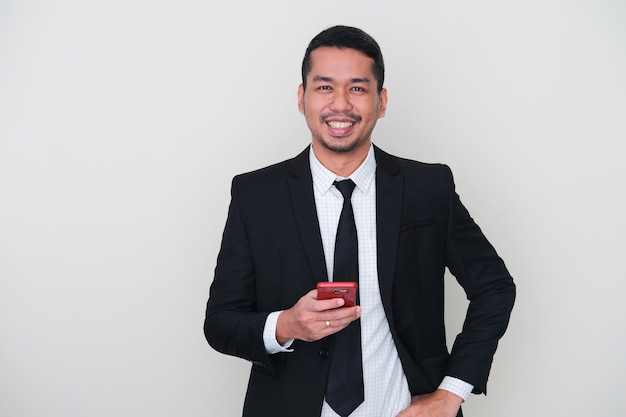 Homem adulto asiático vestindo terno preto e gravata sorrindo enquanto usa o telefone celular