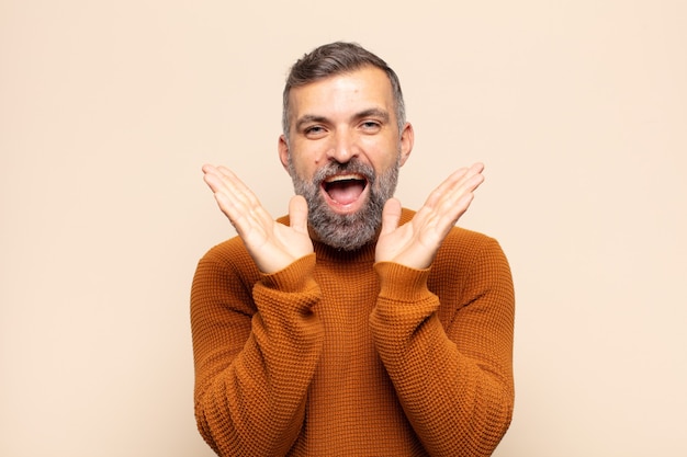 Homem adulto bonito parecendo feliz e animado, chocado com uma surpresa inesperada com as duas mãos abertas ao lado do rosto