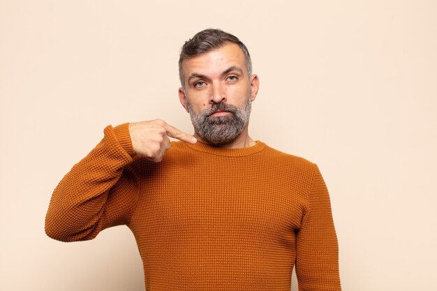 Homem adulto bonito parecendo feliz, orgulhoso e surpreso, apontando alegremente para si mesmo, sentindo-se confiante e elevado