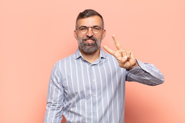 Homem adulto bonito sorrindo e parecendo amigável, mostrando o número dois ou o segundo com a mão para a frente, em contagem regressiva