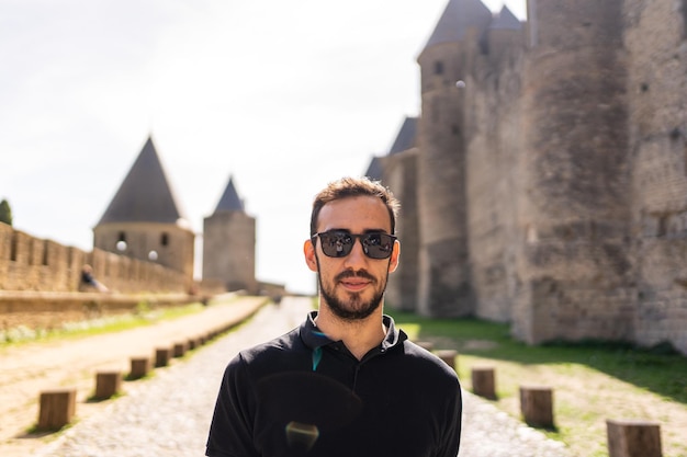 Homem adulto caucasiano em pé em um caminho ao lado da parede de um castelo medieval. França