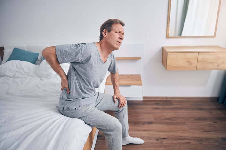 Foto homem adulto chateado, mantendo os olhos fechados enquanto está sentado na cama, tentando se levantar
