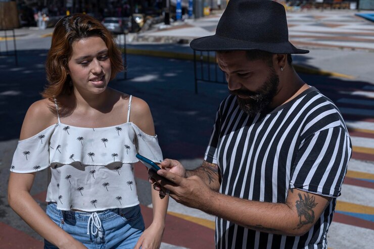 Foto homem adulto com barba e chapéu com jovem latino-americana andando por uma cidade de férias usando o mapa em seu celular para guiá-lo conceito de férias