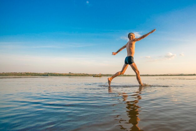 Homem adulto com um moicano na cabeça e shorts pretos correndo na água