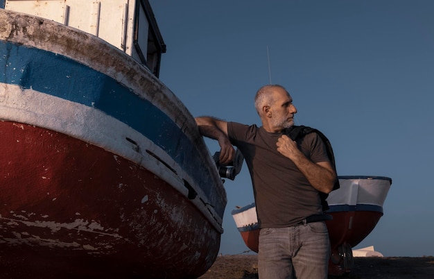 Homem adulto de pé na praia com um barco de pesca durante o pôr do sol Almeria Espanha