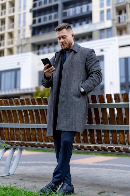 Homem adulto de terno em pé perto do banco com telefone. Empresário focado em trabalho ou trabalho por telefone.
