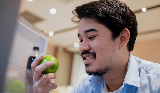 Foto homem adulto do oriente médio abre a geladeira para encontrar maçã verde após terminar o jantar