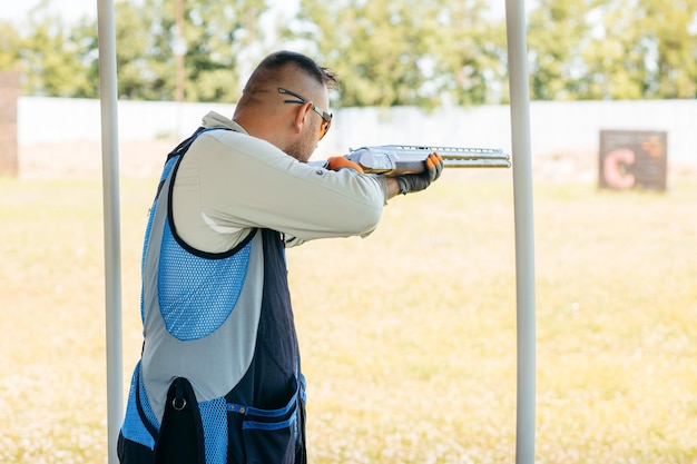 Foto homem adulto em óculos de sol e um colete de rifle praticando tiro com arma de fogo