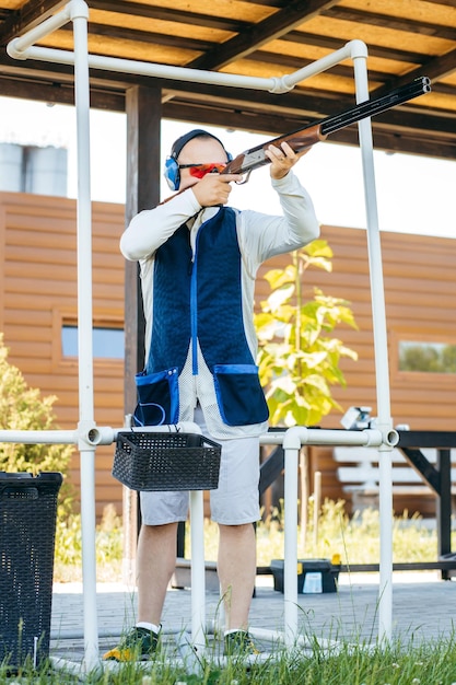 Homem adulto em óculos de sol e um colete de rifle praticando tiro com arma de fogo