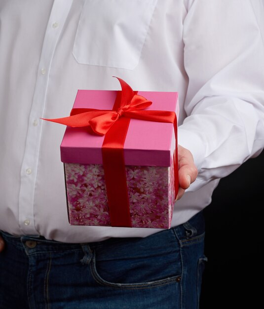 Homem adulto em uma camisa branca segura uma caixa de papelão de presente rosa com um laço