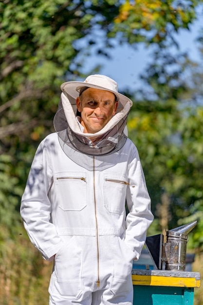 Foto homem adulto em uniforme protetor em pé perto de colméias. apicultor fazendo seu trabalho com colheita de mel.