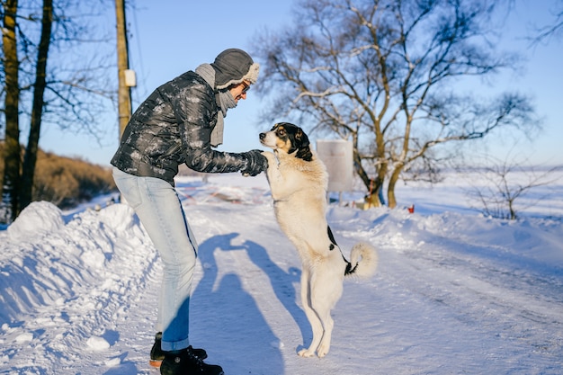 Homem adulto feliz posando com um cachorro amigável na estrada de neve