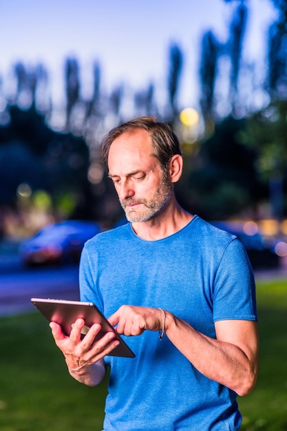 Homem adulto hispânico ao ar livre com tecnologia de tablet digital lendo e trabalhando empresário