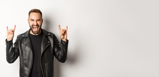 Homem adulto legal na jaqueta de couro preta mostrando rock no gesto e na língua curtindo o festival de música st