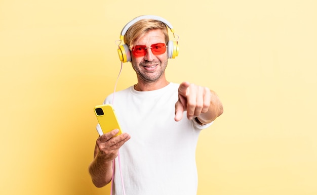 Homem adulto loiro apontando para a câmera e escolhendo você com fones de ouvido