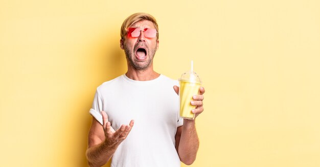 Homem adulto loiro parecendo desesperado, frustrado e estressado com um milkshake