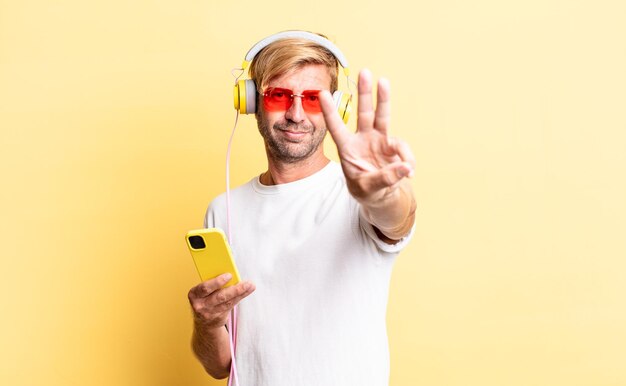 Homem adulto loiro sorrindo e parecendo amigável, mostrando o número três com fones de ouvido