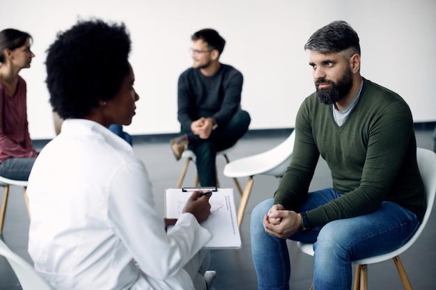 Homem adulto médio conversando com psicoterapeuta feminina durante reunião de grupo