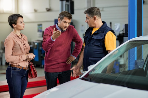 Homem adulto médio falando sobre avaria do veículo com seu mecânico de automóveis em uma oficina