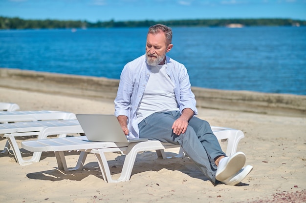 Homem adulto sério com laptop na praia