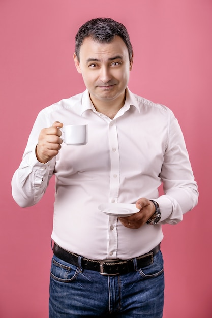 Homem adulto sorridente com uma xícara de café, olhando para a câmera contra de rosa isolado