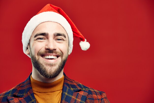 Foto homem adulto sorridente, usando chapéu de papai noel no vermelho