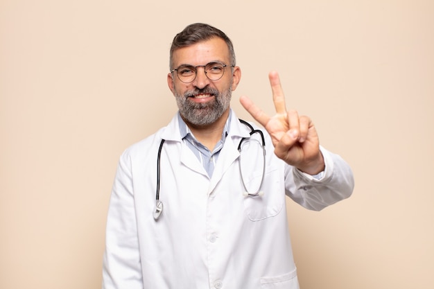 Homem adulto sorrindo e parecendo amigável, mostrando o número dois ou o segundo com a mão para a frente, em contagem regressiva