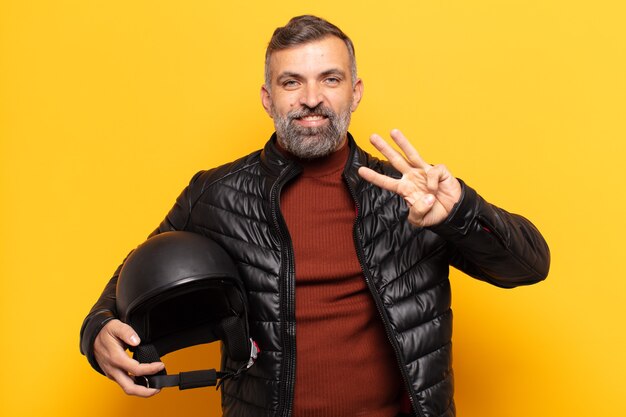 Homem adulto sorrindo e parecendo amigável, mostrando o número três ou terceiro com a mão para a frente, em contagem regressiva