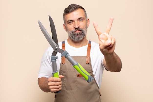 Homem adulto sorrindo e parecendo feliz, despreocupado e positivo, gesticulando vitória ou paz com uma das mãos