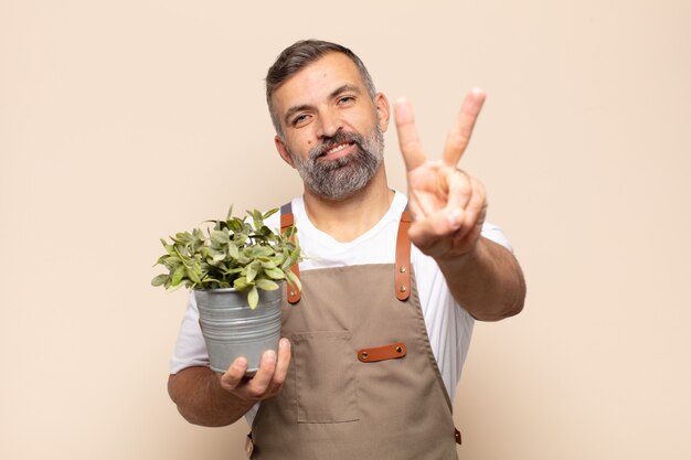 Homem adulto sorrindo e parecendo feliz, despreocupado e positivo, gesticulando vitória ou paz com uma das mãos