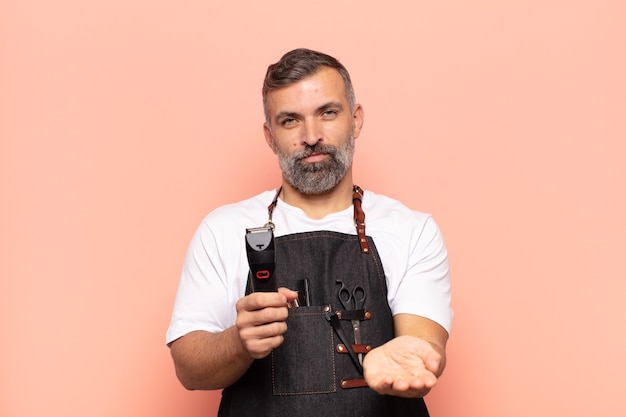 Homem adulto sorrindo feliz com um olhar amigável, confiante e positivo, oferecendo e mostrando um objeto ou conceito