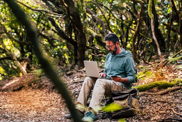 Homem adulto trabalhando com computador laptop no meio da floresta verde selvagem