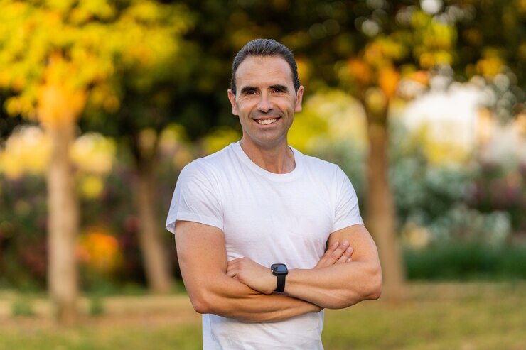 Homem adulto vestindo roupas esportivas brancas treinando no parque. Ele está sorrindo e olhando para a câmera.