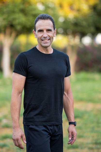 Homem adulto vestindo roupas esportivas pretas, treinando no parque. Ele está sorrindo e olhando para a câmera.