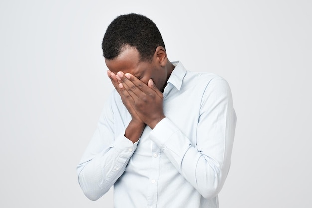 Homem africano adulto com expressão triste, cobrindo o rosto com as mãos enquanto chora