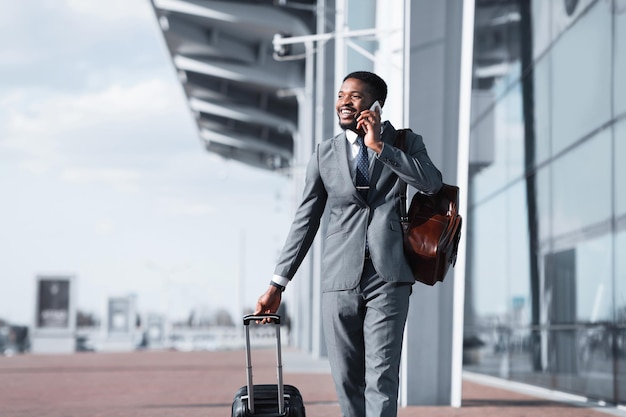 Homem africano andando com bagagem e falando ao telefone