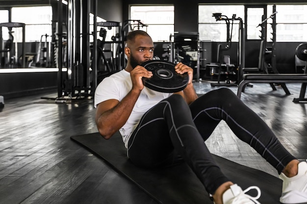 Homem africano bonito em roupas esportivas fazendo flexões com damblebell nas mãos no ginásio