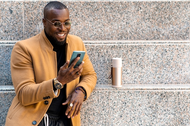 Homem africano bonito em um terno da moda elegante sorrindo conversando no smartphone encostado em uma parede.