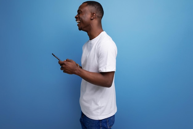 Homem africano casual com corte de cabelo curto em camiseta branca conversando enquanto segura o smartphone na mão