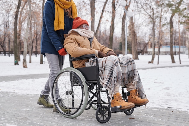 Homem africano com deficiência, sentado em uma cadeira de rodas, caminhando em um dia de inverno junto com seu assistente