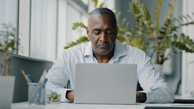 Homem africano concentrado, especialista focado em funcionário americano, sentado no escritório, trabalhando em laptop