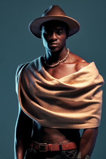 Homem africano de retrato com um xale e contra um fundo azul Roupas de cultura séria ou orgulhosa e modelo de moda masculina negra com uma pose de chapéu contra um pano de fundo de estúdio com espaço de maquete