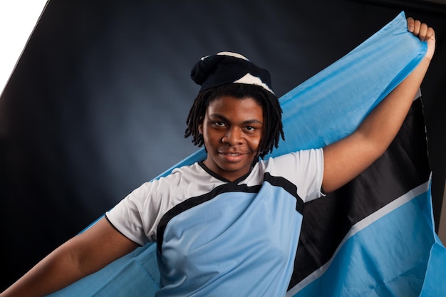 Homem africano do Botswana com uma bandeira sorrindo em um estúdio fotográfico contra um fundo escuro