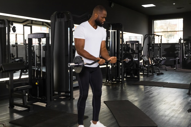 Homem africano em forma e musculoso levantando peso pesado de barra no ginásio